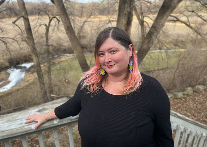 woman with brown and pink hair wearing a black long sleeved shirt posing in front of nature scenery